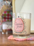 Candle labeled 'Cinnamon Mousse' on a wooden surface with a blurred background