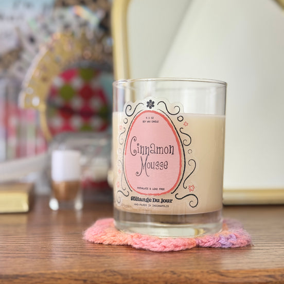 Candle labeled 'Cinnamon Mousse' on a wooden surface with a blurred background